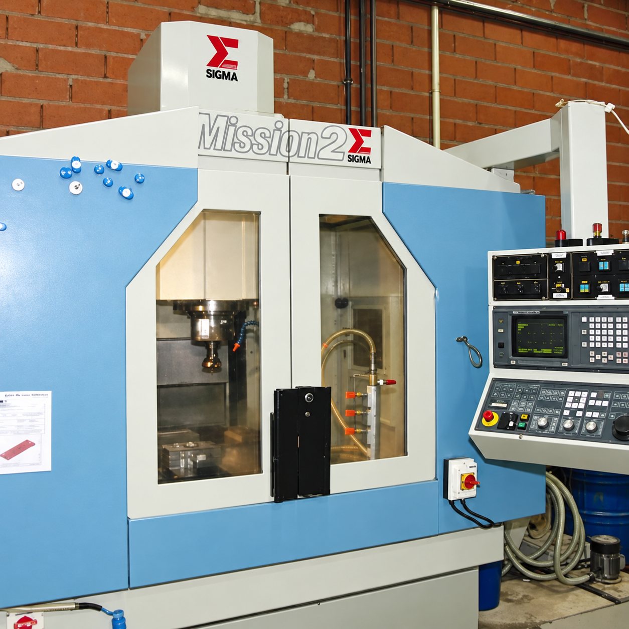 Machine-outil CNC bleue et blanche de marque Sigma, modèle Mission 2, avec son pupitre de commande dans un atelier aux murs de briques.