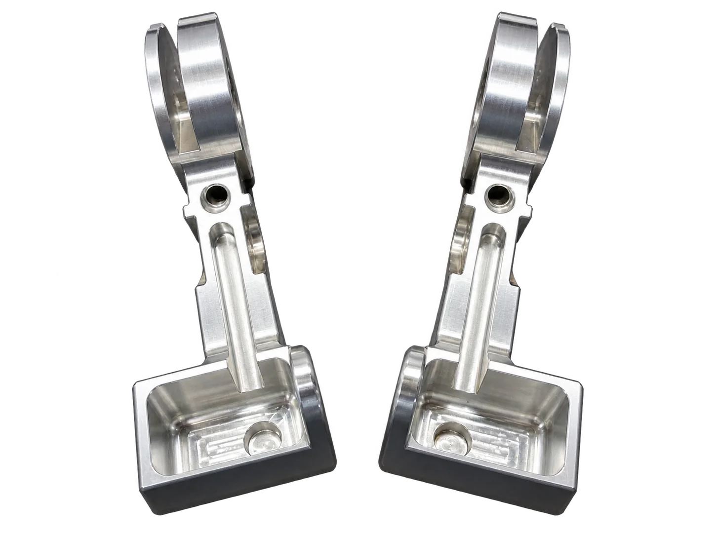 Deux pièces mécaniques en aluminium usiné et poli, symétriques, posées côte à côte sur un plan de travail gris foncé.