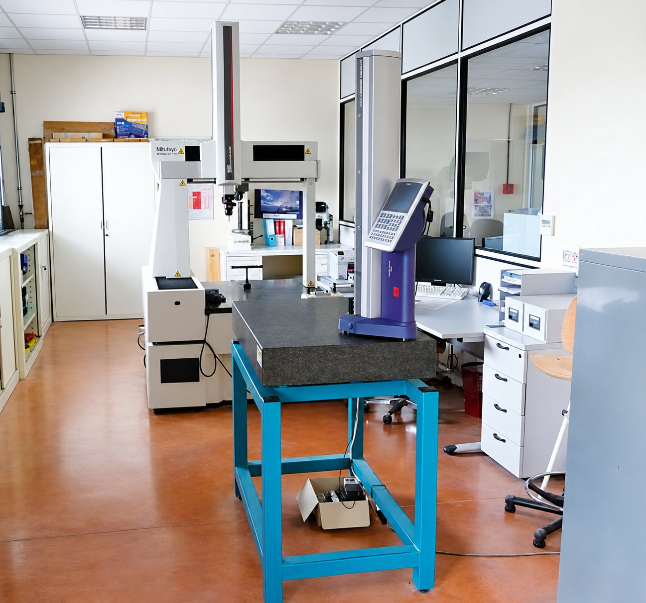Un laboratoire de métrologie équipé d'une machine à mesurer tridimensionnelle, d'un marbre noir posé sur une table bleue et d'un poste de travail informatique.